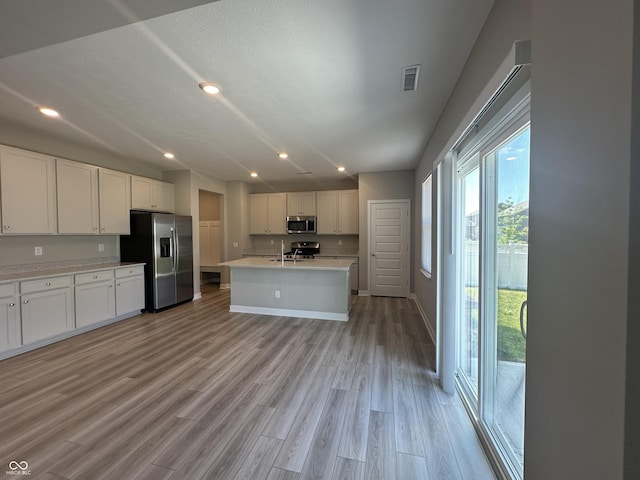 kitchen with light wood-type flooring, appliances with stainless steel finishes, a kitchen island with sink, and white cabinets