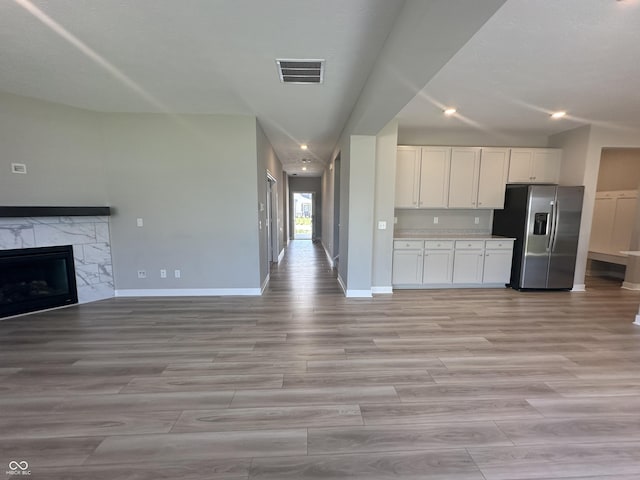 kitchen with stainless steel refrigerator with ice dispenser, white cabinetry, a fireplace, and light wood-type flooring