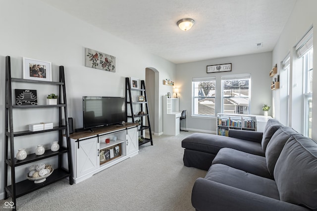 living room featuring a textured ceiling, baseboards, arched walkways, and light colored carpet