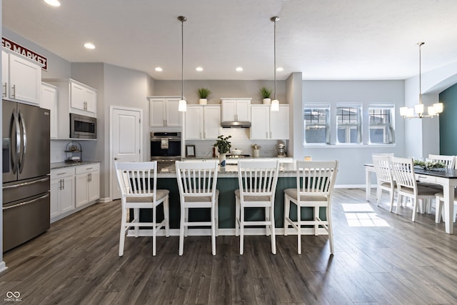 kitchen with appliances with stainless steel finishes, a center island with sink, hanging light fixtures, a kitchen bar, and white cabinets