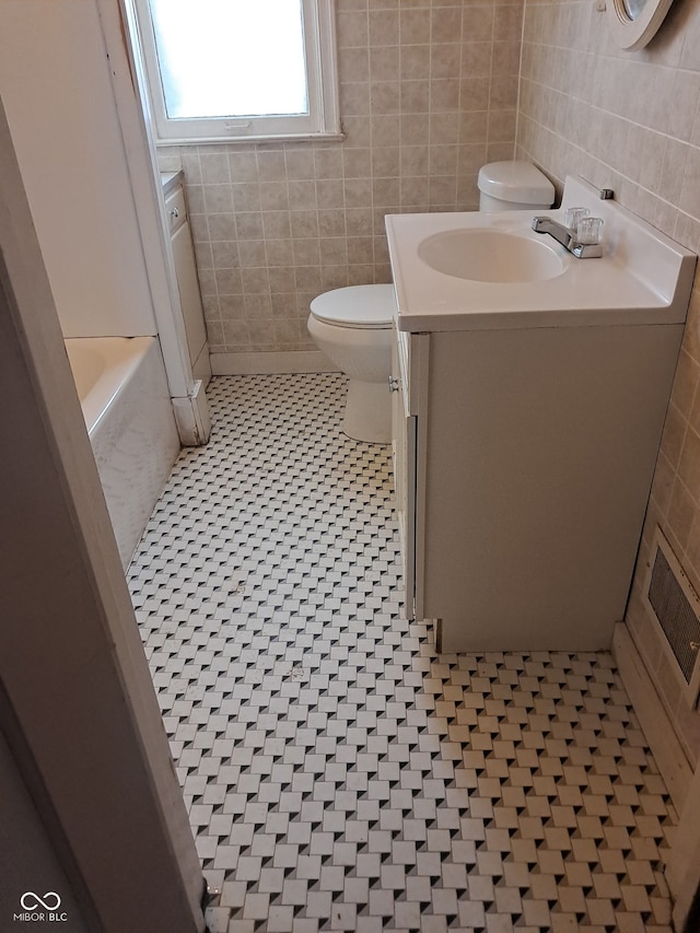 bathroom featuring tile walls, a bathtub, vanity, toilet, and tile patterned floors