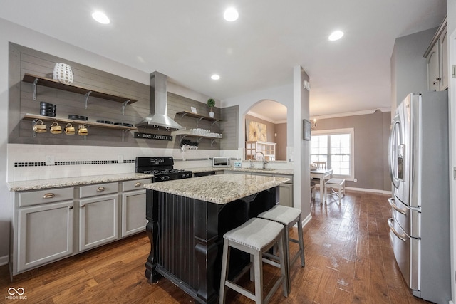 kitchen with black range with gas cooktop, a breakfast bar, a center island, stainless steel fridge, and exhaust hood