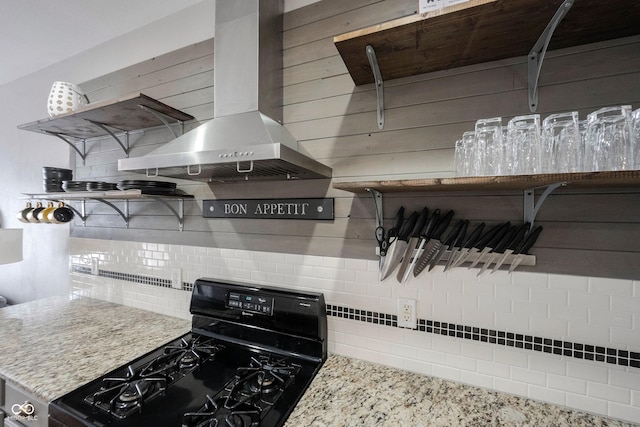 kitchen with light stone counters, black range with gas cooktop, decorative backsplash, and wall chimney range hood