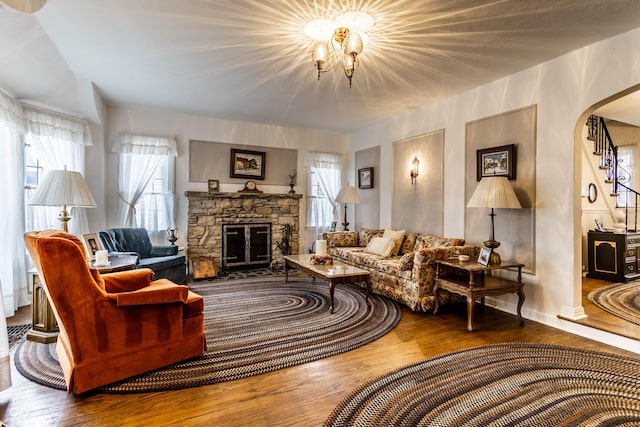 living room featuring hardwood / wood-style flooring, a stone fireplace, and a notable chandelier