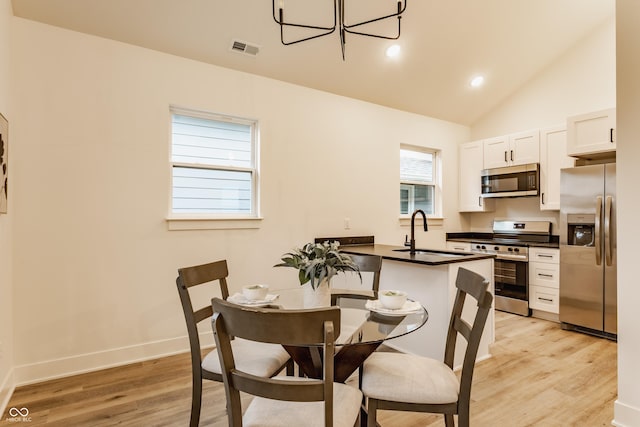 dining space with lofted ceiling, sink, and light hardwood / wood-style flooring