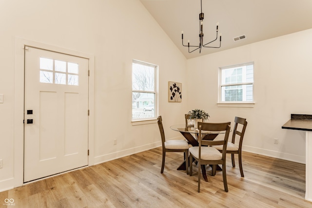 dining area featuring high vaulted ceiling, a wealth of natural light, an inviting chandelier, and light hardwood / wood-style flooring