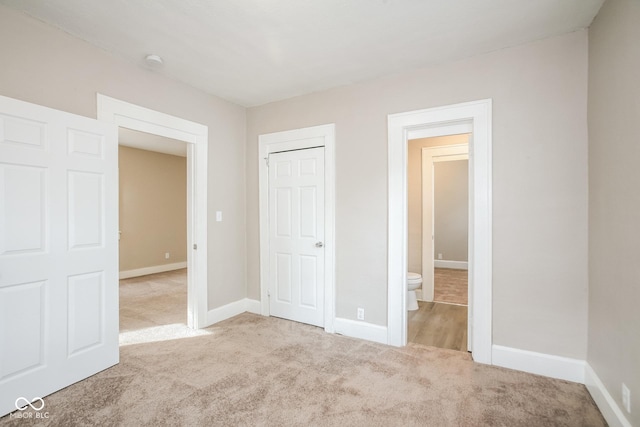 unfurnished bedroom featuring light colored carpet, a closet, and ensuite bathroom