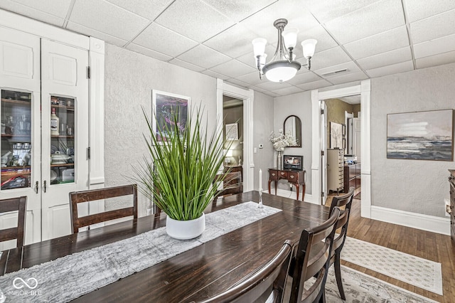 dining area featuring a drop ceiling, wood-type flooring, and an inviting chandelier