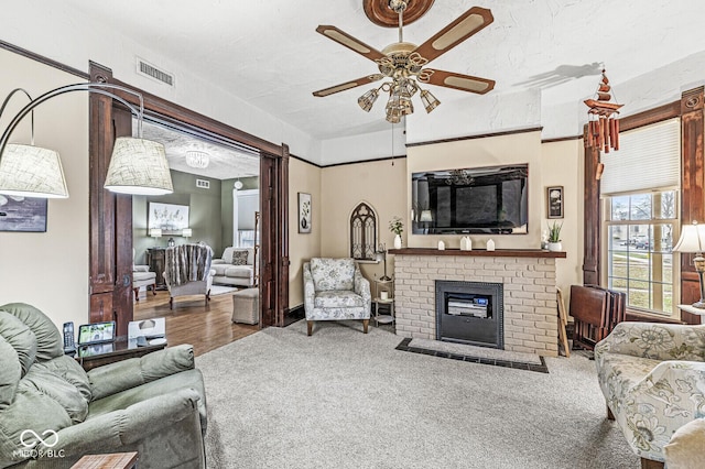 carpeted living room with a brick fireplace, a textured ceiling, and ceiling fan