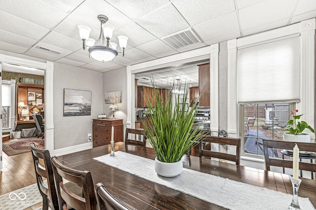 dining room with hardwood / wood-style floors, a drop ceiling, and a notable chandelier