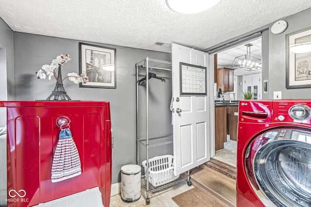 clothes washing area with washer / clothes dryer, a notable chandelier, sink, and a textured ceiling