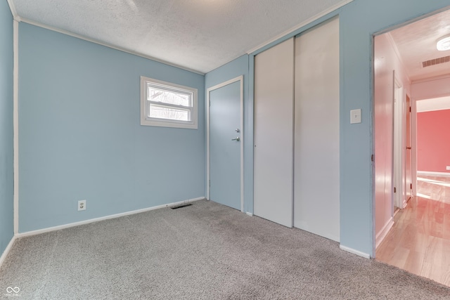 unfurnished bedroom featuring light carpet, a closet, and a textured ceiling