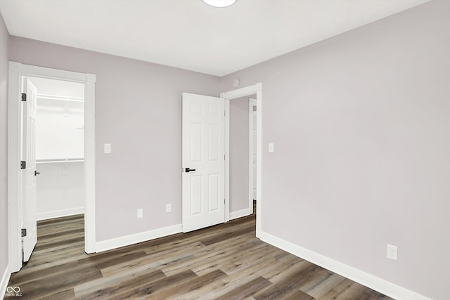 unfurnished bedroom with a spacious closet, dark wood-type flooring, and a closet