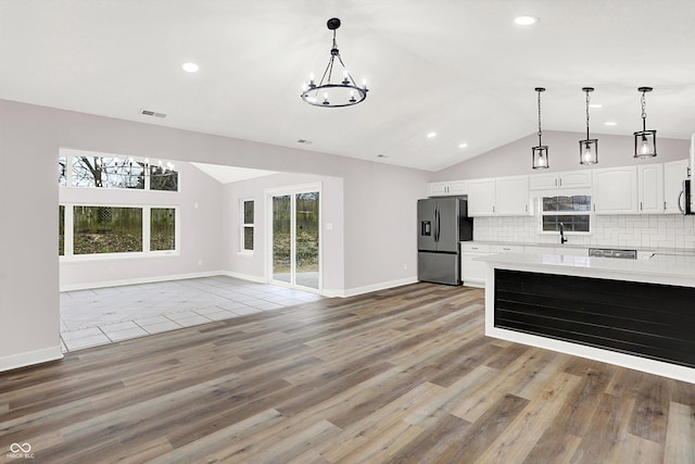 kitchen featuring lofted ceiling, white cabinetry, hanging light fixtures, stainless steel fridge, and backsplash