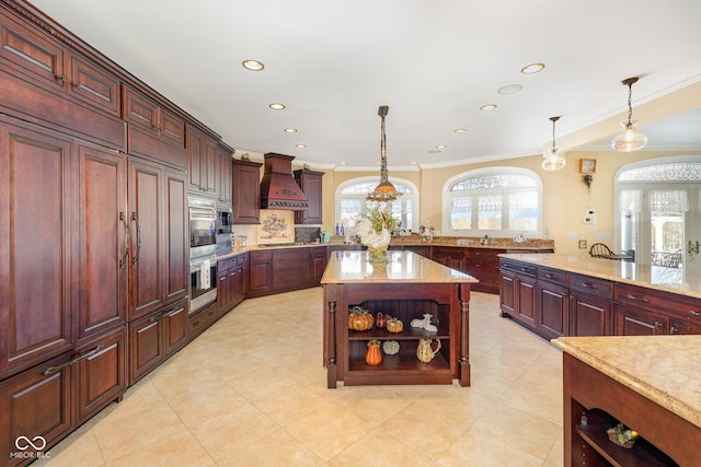 kitchen with decorative light fixtures, a center island, ornamental molding, custom range hood, and light stone countertops