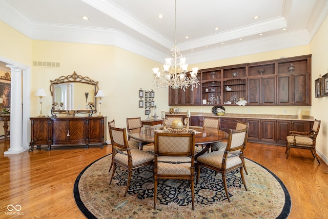 dining room featuring decorative columns, ornamental molding, a notable chandelier, a raised ceiling, and light wood-type flooring