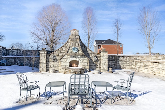 snow covered patio with an outdoor stone fireplace