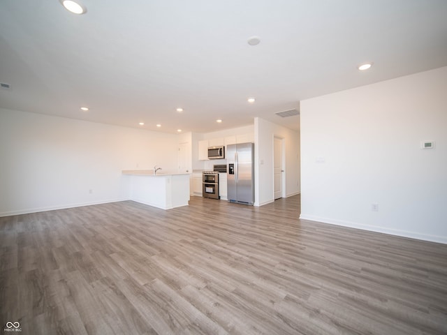 unfurnished living room with recessed lighting, visible vents, baseboards, and wood finished floors