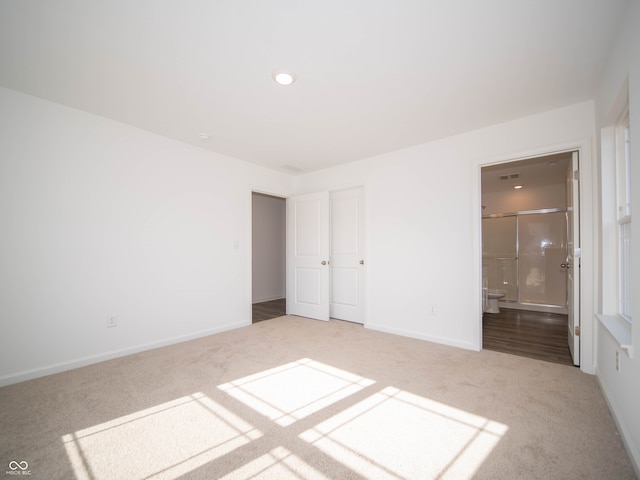 unfurnished bedroom with ensuite bath, carpet, visible vents, and baseboards