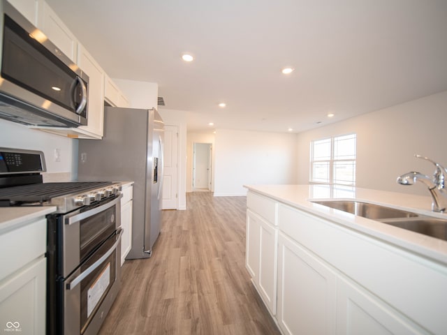 kitchen featuring light wood finished floors, appliances with stainless steel finishes, white cabinets, and a sink