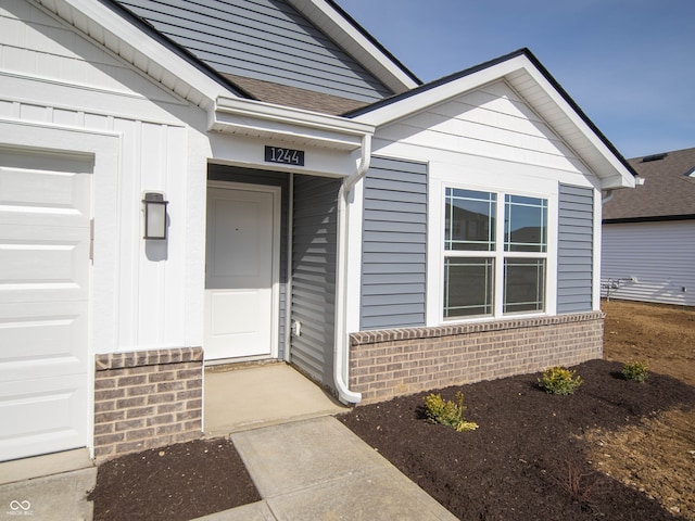 entrance to property with a garage, a shingled roof, and brick siding