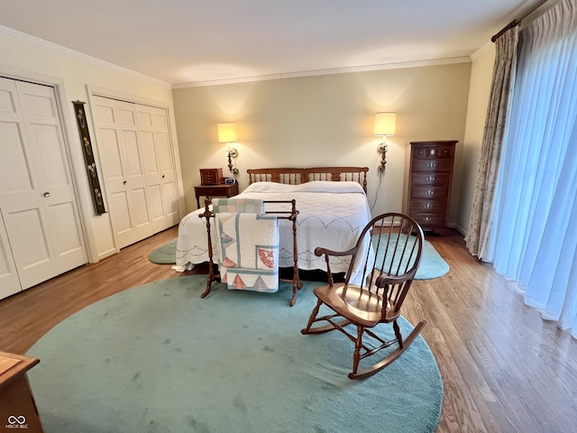 bedroom featuring hardwood / wood-style flooring, crown molding, and two closets