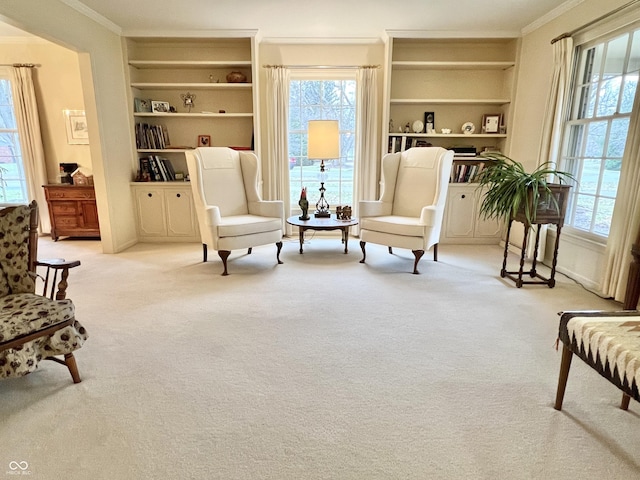 sitting room with built in shelves, ornamental molding, light colored carpet, and a healthy amount of sunlight