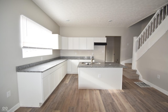 10 N Keystone Ave, Indianapolis, IN 46201 - kitchen with wood-type flooring, sink, dark stone countertops, white cabinets, and a center island with sink