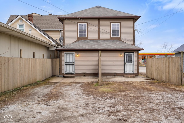 rear view of property with entry steps, fence, and roof with shingles