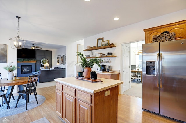 kitchen with a kitchen island, ceiling fan with notable chandelier, hanging light fixtures, stainless steel refrigerator with ice dispenser, and light hardwood / wood-style flooring