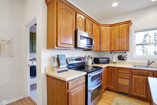 kitchen featuring stainless steel appliances, sink, light wood-type flooring, and washer / clothes dryer