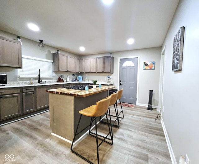 kitchen with butcher block counters, sink, a center island, light wood-type flooring, and a kitchen breakfast bar