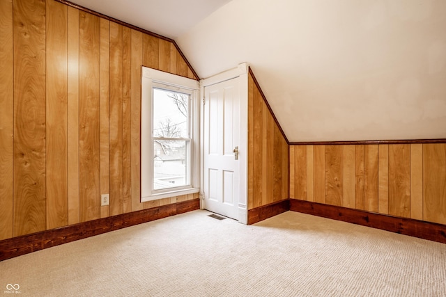 bonus room with vaulted ceiling, light carpet, and wooden walls