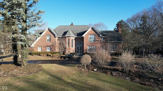 traditional home featuring brick siding, a chimney, and a front yard