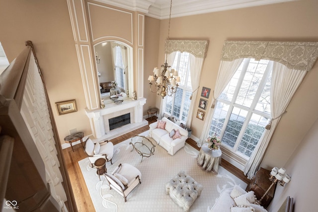 living area with baseboards, a glass covered fireplace, ornamental molding, wood finished floors, and an inviting chandelier