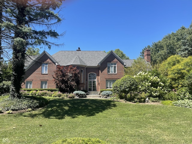 view of front of home with brick siding, a chimney, and a front yard