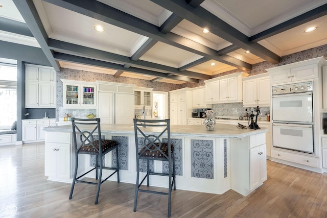 kitchen with light wood-type flooring, double oven, a kitchen bar, and white cabinetry