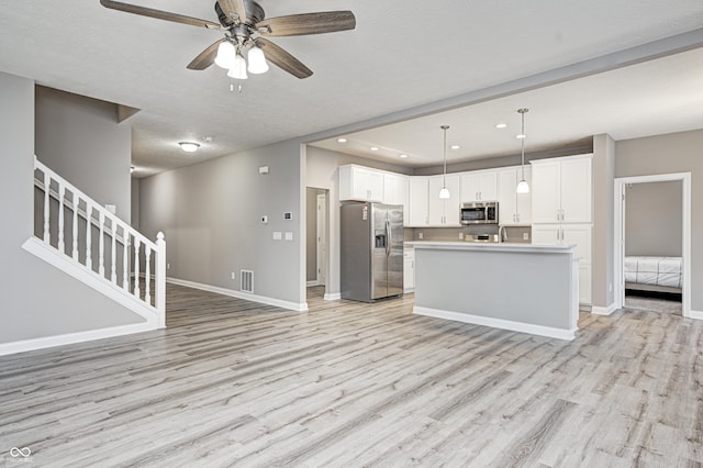 kitchen featuring light wood finished floors, baseboards, white cabinets, open floor plan, and stainless steel appliances