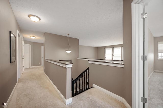 hall featuring an upstairs landing, a textured ceiling, baseboards, and carpet floors