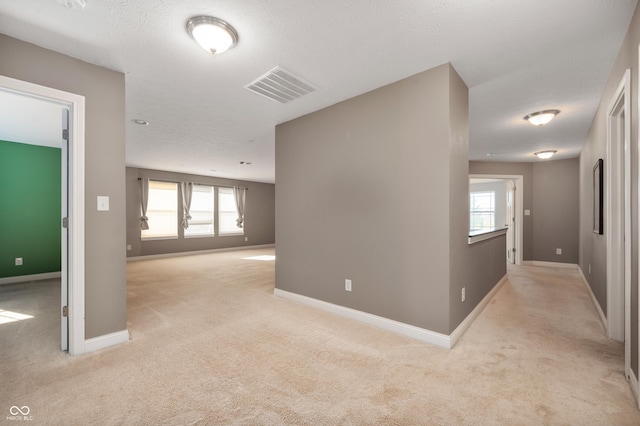 unfurnished room with visible vents, light colored carpet, and baseboards