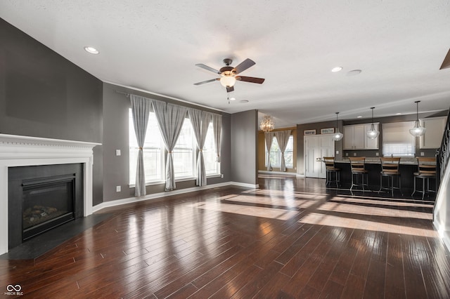 unfurnished living room featuring a ceiling fan, a glass covered fireplace, wood finished floors, recessed lighting, and baseboards