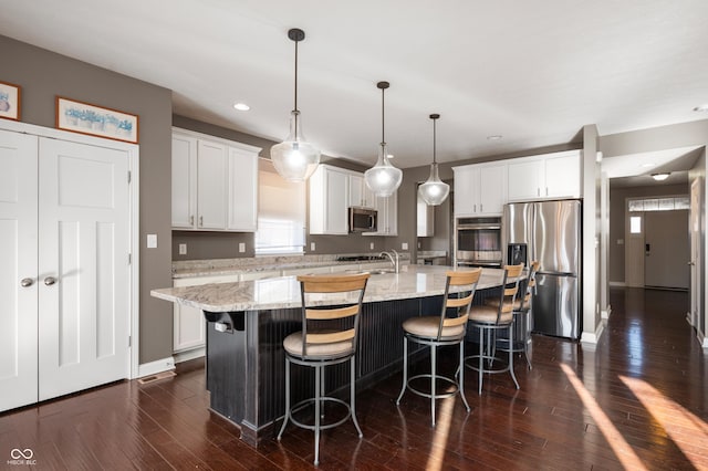 kitchen featuring a breakfast bar, a kitchen island with sink, dark wood-type flooring, appliances with stainless steel finishes, and white cabinetry