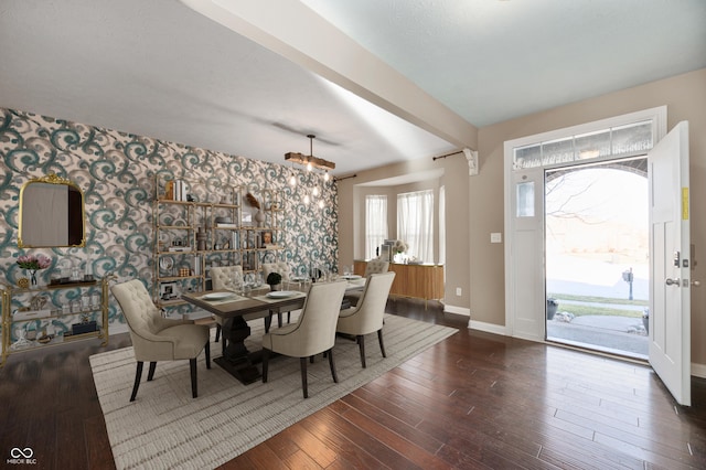 dining room featuring wallpapered walls, beamed ceiling, wood finished floors, and baseboards