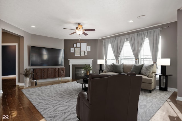 living area with a glass covered fireplace, baseboards, ceiling fan, and wood finished floors