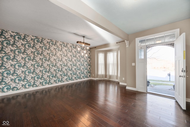 foyer with beamed ceiling, wallpapered walls, baseboards, a chandelier, and dark wood-style flooring