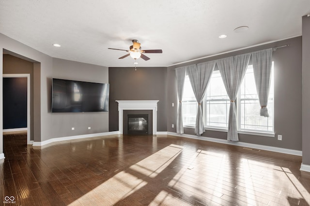 unfurnished living room featuring a glass covered fireplace, baseboards, wood finished floors, and a ceiling fan