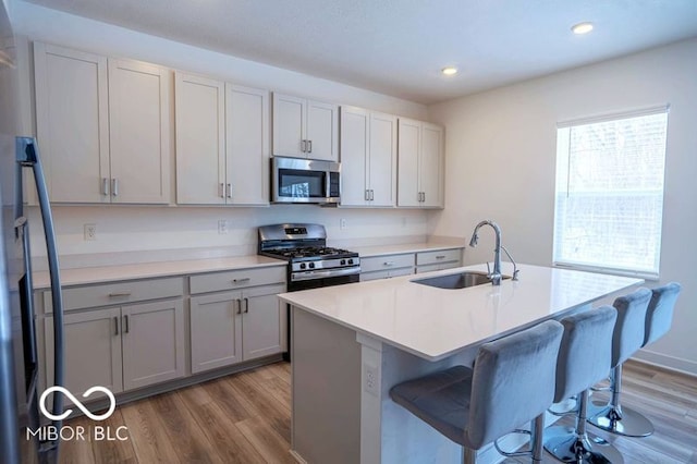 kitchen with stainless steel appliances, light countertops, gray cabinetry, a kitchen island with sink, and a sink