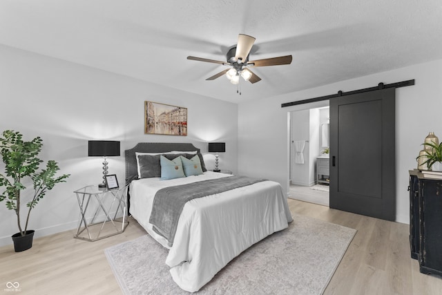 bedroom with connected bathroom, a textured ceiling, ceiling fan, a barn door, and light hardwood / wood-style floors