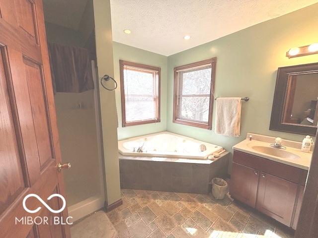 bathroom featuring a stall shower, a jetted tub, vanity, and a textured ceiling