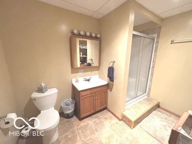 bathroom with toilet, a shower stall, vanity, a drop ceiling, and baseboards